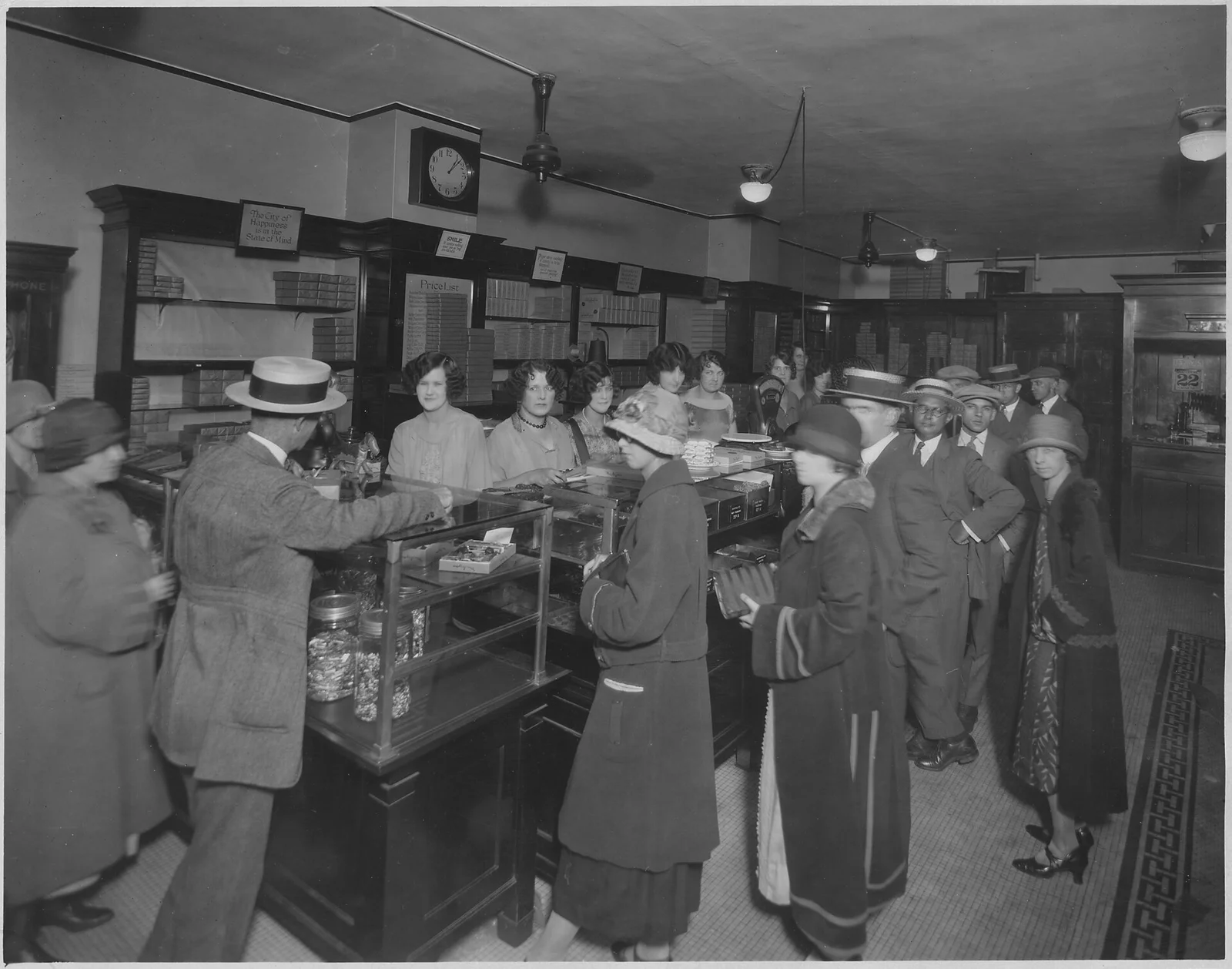 Clienti in fila al bancone di un negozio di dolciumi nel 1927, con le commesse dietro il banco